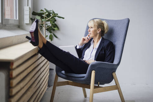 Nachdenkliche reife Geschäftsfrau sitzt mit Laptop auf einem Sessel - JOSEF23892
