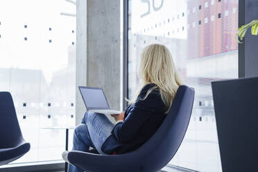 Blonde reife Geschäftsfrau sitzt mit Laptop auf einem Stuhl - JOSEF23909