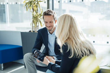 Smiling businessman sitting with businesswoman holding tablet PC in office - JOSEF23922