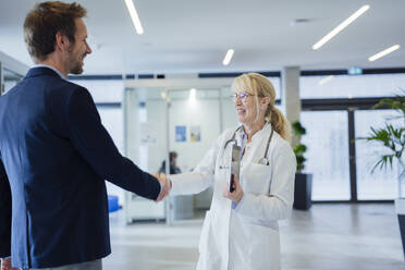 Happy mature doctor shaking hands with man in hospital - JOSEF23953