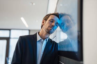 Businessman leaning on computer screen with eyes closed in office - JOSEF23957