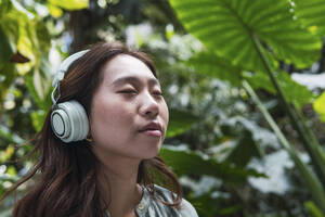 Frau, die mit geschlossenen Augen über drahtlose Kopfhörer Musik hört - PNAF06168