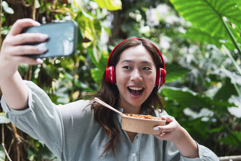 Happy woman taking selfie with food container - PNAF06173