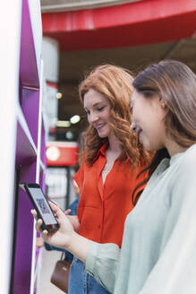 Lächelnde Freunde mit Smartphones in der Nähe eines Fahrkartenautomaten - PNAF06184