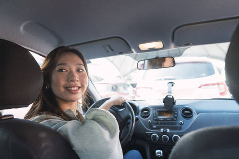 Lächelnde Frau, die im Auto sitzend über die Schulter schaut - PNAF06199