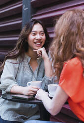 Lächelnde Frau trinkt Kaffee und unterhält sich mit einem Freund in einem Straßencafé - PNAF06209