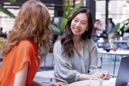 Lächelnde Frau im Gespräch mit einem Freund im Cafe - PNAF06212