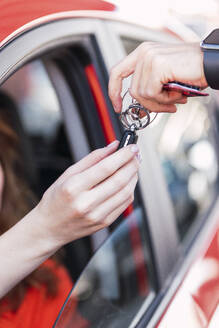 Hand einer Frau, die den Autoschlüssel von einem Verkäufer entgegennimmt - PNAF06223