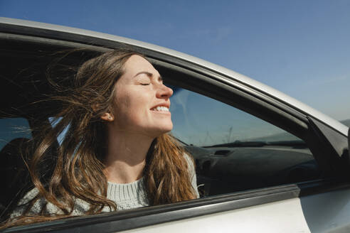 Russia, Rostov-on-don, portrait of a beautiful happy long-haired woman looking out of an open car window, long hair curling in the wind - KVBF00078