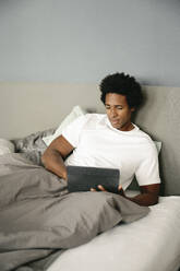 Germany, young handsome man using tablet in bed - FLMZF00007