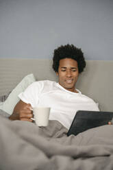 Germany, happy man reading in bed - FLMZF00009