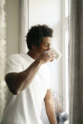 Germany, young man drinking coffee, looking out of window - FLMZF00022