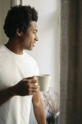 Germany, young man drinking coffee at home - FLMZF00023