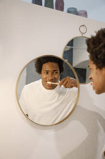 Man brushing teeth looking at reflection on mirror in bathroom - FLMZF00024