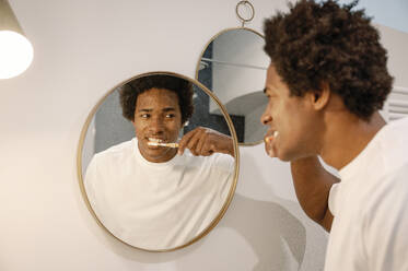Man brushing teeth looking at mirror reflection in bathroom - FLMZF00025