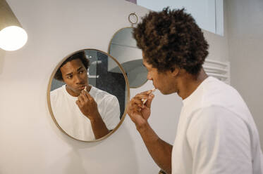 Man brushing teeth looking at mirror in bathroom - FLMZF00026
