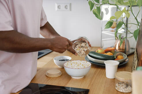 Man preparing breakfast cereal in bowl at kitchen counter - FLMZF00027