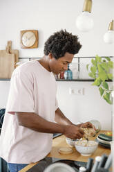 Germany, young afro American man preparing musli - FLMZF00028