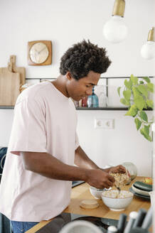 Man preparing breakfast muesli in bowl at kitchen counter - FLMZF00028