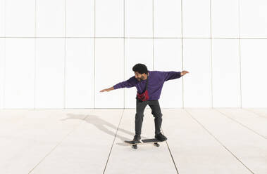 Portugal, young man riding a skateboard against the white minimalistic tile wall - VRAF00474
