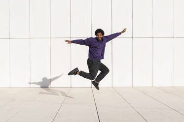 Portugal, young man jumping against the minimalistic white tile wall - VRAF00481