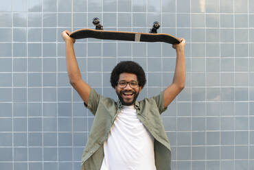 Portugal, young funny man holding a skateboard against the blue tile wall - VRAF00488