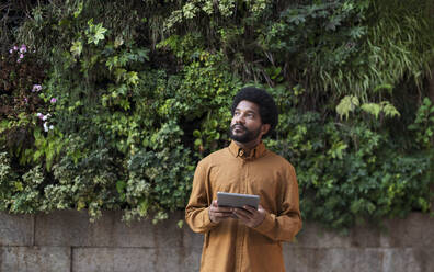 Portugal, young man using a tablet against the natural plants wall background - VRAF00493