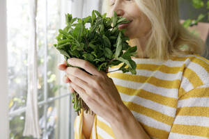 Mature woman smelling fresh mint at home - TYF00810