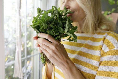 Mature woman smelling fresh mint at home - TYF00810