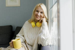 Happy woman holding mug and sitting on sofa at home - TYF00816