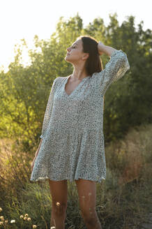 Young woman wearing sundress and standing in field - ALKF01105