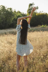 A woman stands in a field with her arms up in the air - ALKF01106