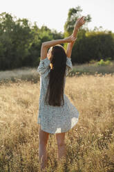 Carefree woman standing with arms raised in meadow - ALKF01106