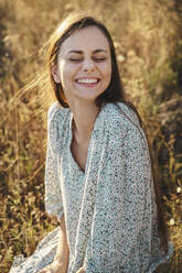 Happy woman sitting with eyes closed in meadow - ALKF01107