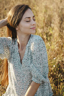 Beautiful woman sitting with eyes closed in meadow - ALKF01108