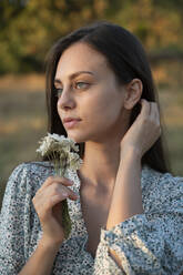 Beautiful young woman holding wildflower near face - ALKF01115