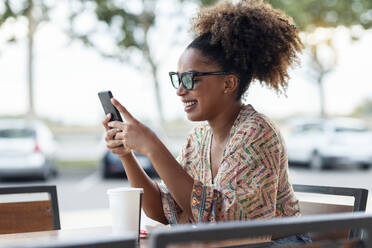 Happy woman using smart phone at sidewalk cafe - JSRF02915