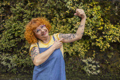 Smiling redhead senior woman flexing muscles with tattoo on it - ALZF00008