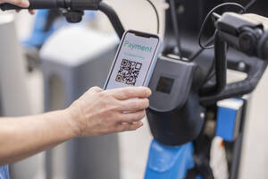 Hands of woman paying for renting bicycle through smart phone - ALZF00018