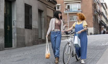 Woman talking to mother with bicycle on street in city - ALZF00029