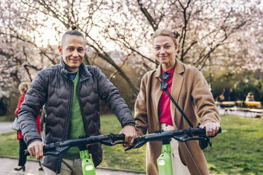 A couple portrait with scooters around the city, mobility, sustainability, eco transport - TILF00093