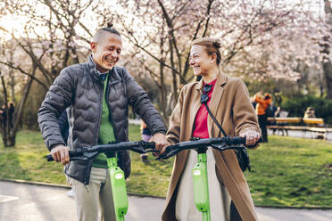 A couple portrait with scooters around the city, mobility, sustainability, eco transport - TILF00094