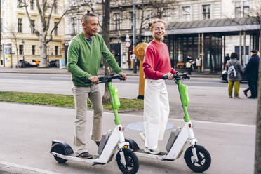 Couple riding electric push scooter on footpath in city - TILF00095