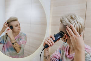 Frau beim Trimmen der Haare mit einem elektrischen Rasierapparat im Badezimmer zu Hause - YTF02055