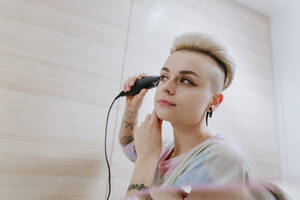 Hipster-Frau beim Trimmen der Haare mit einem elektrischen Rasierapparat zu Hause - YTF02057