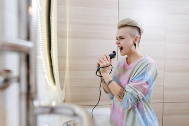 Young woman singing while cutting hair with electric razor in bathroom, woman, mirror, care, beauty, home, hairstyle, millennials, individuality, happy, tattoo, fun, - YTF02061