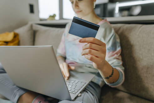 Frau mit Kreditkarte und Laptop auf dem Sofa zu Hause - YTF02069