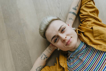 Portrait of young woman lying on floor looking at camera, woman, hairstyle, millennials, individuality, tattoo, relax - YTF02082