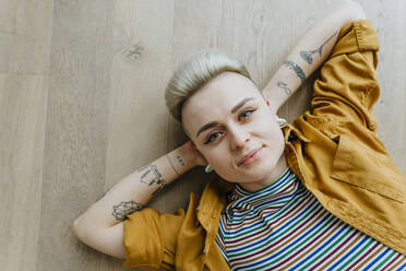 Portrait of young woman lying on floor looking at camera, woman, hairstyle, millennials, individuality, tattoo, relax - YTF02083