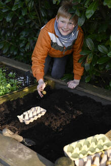 garden, AltesLand, Hamburg, Germany, gardeninglife, spring, springtime, potatoes, boy, 10years, put potatoes, egg carton, seedlings, raised bed, self-sufficiency garden, orange, jacket, potting soil - GISF01059